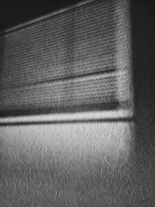 Artistic monochrome of window blinds casting textured shadows on a wall.